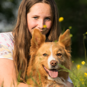 Jeune fille brune, assise dans l'herbe avec un chien beige de typer berger entre ses jambes - Seul on va vite, ensemble on va plus loin